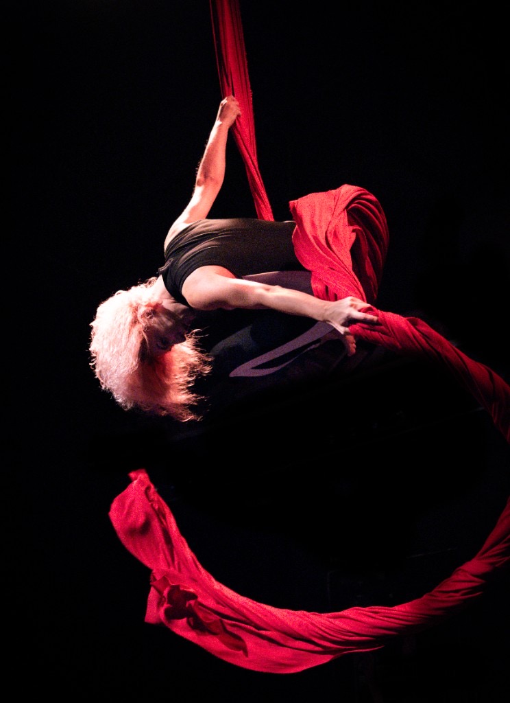 Aerial silk artist wrapped in red silks, dynamic motion