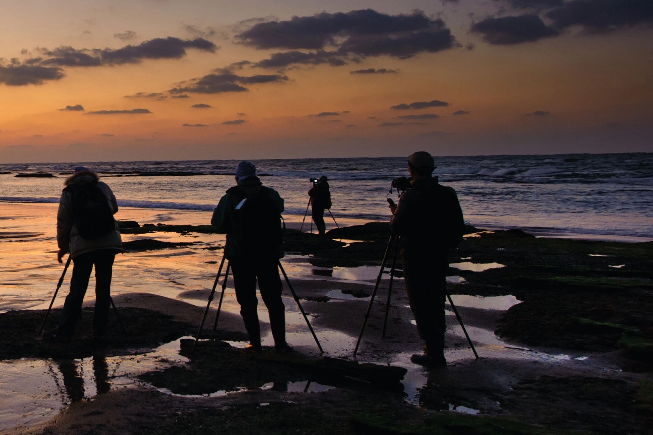 Photographers with tripods on a rocky beach at sunset