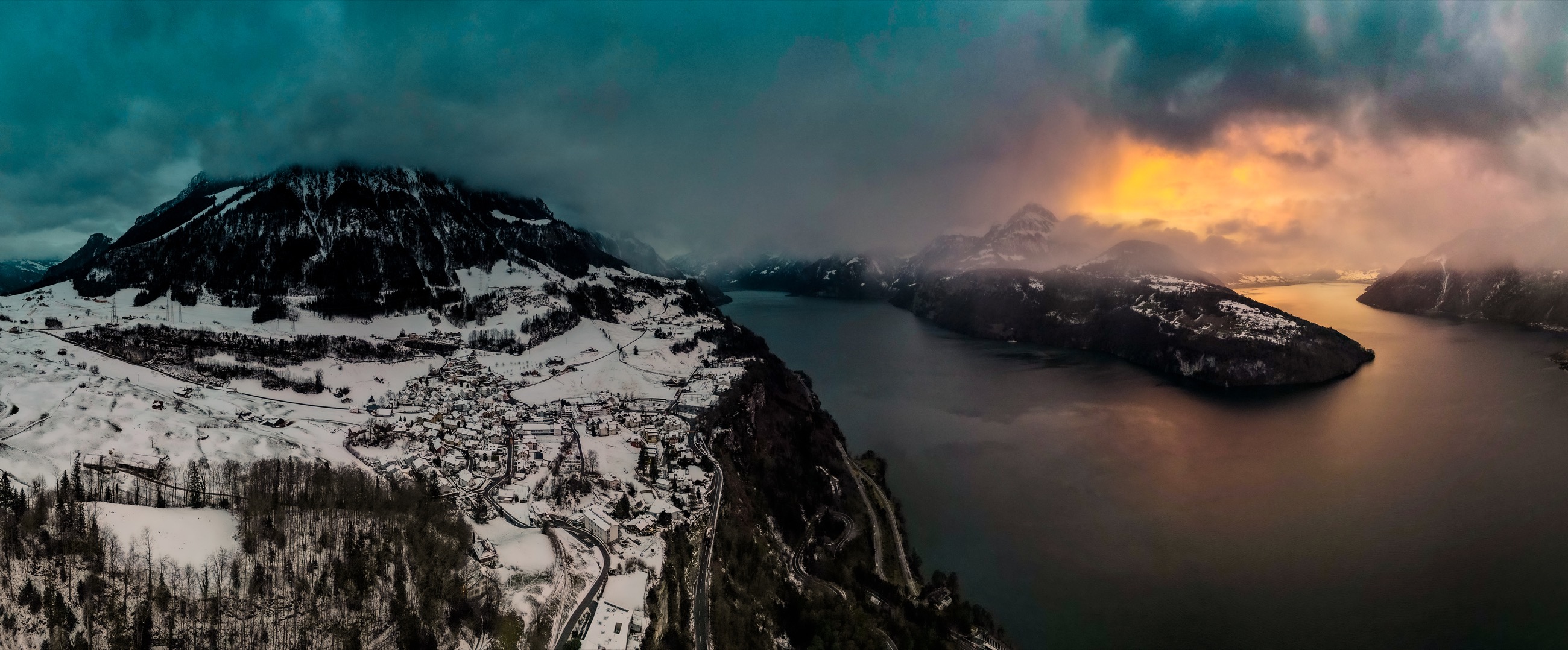 Snow-covered alpine mountains and lake at sunset, aerial panorama